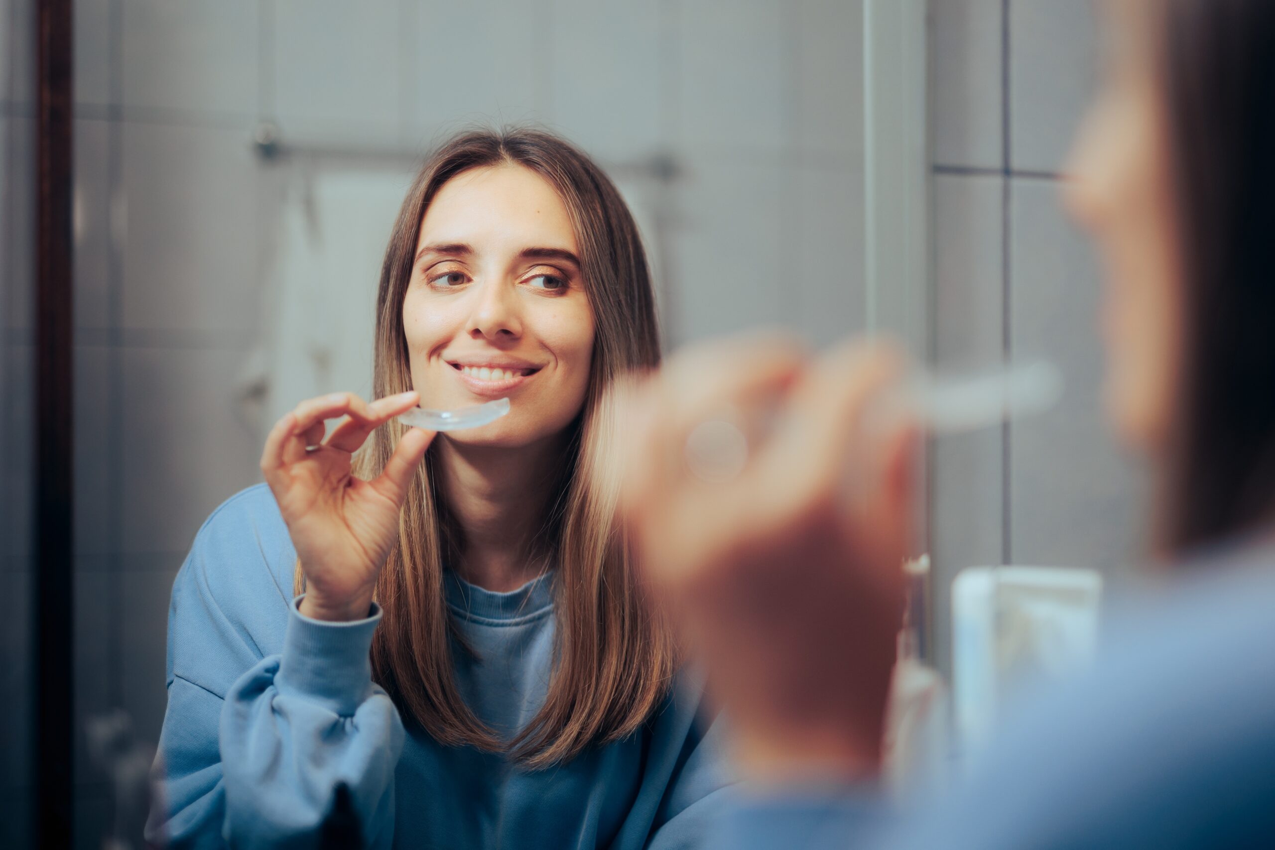 young woman putting in her Invisalign, improved oral health