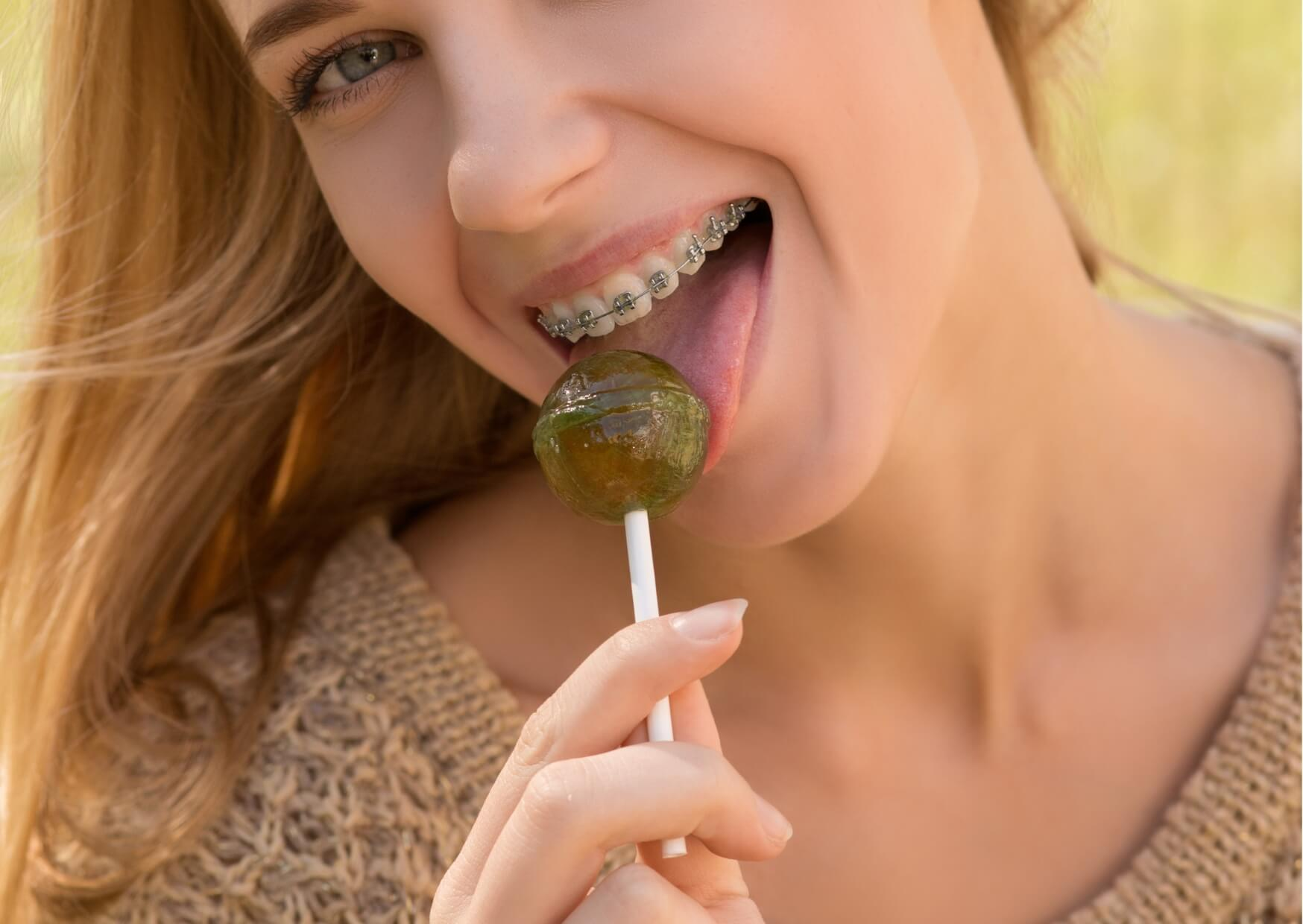 Teen wearing braces eating a lollipop, illustrating why sticky candy can damage braces and should be avoided.