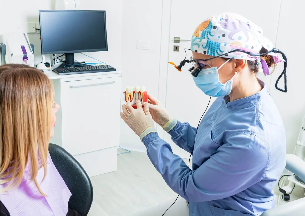 Dentist using a dental implant model to explain the timing of implant placement after a tooth extraction.