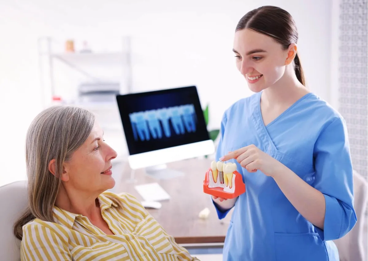 Dental professional explaining the dental implant timeline to a patient using an implant model.