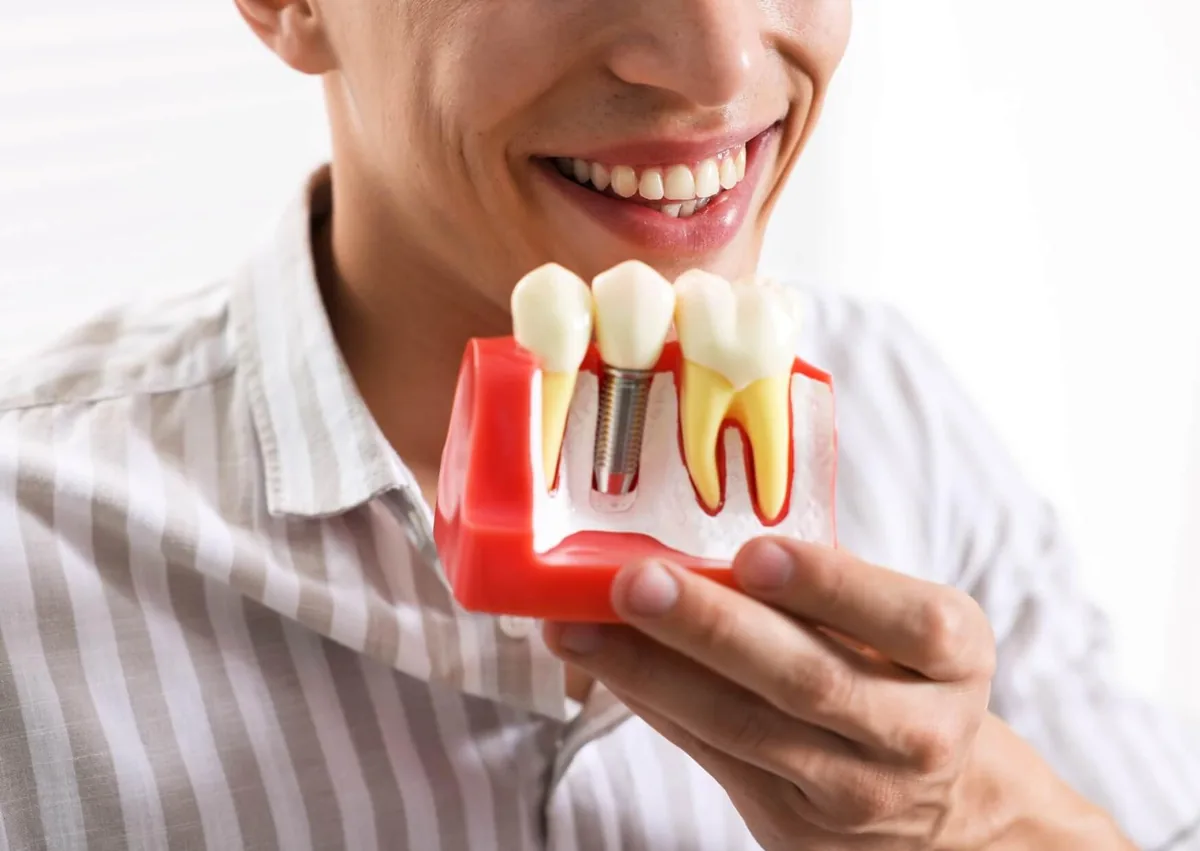 Patient holding a dental implant model while learning about cleaning and caring for dental implants.