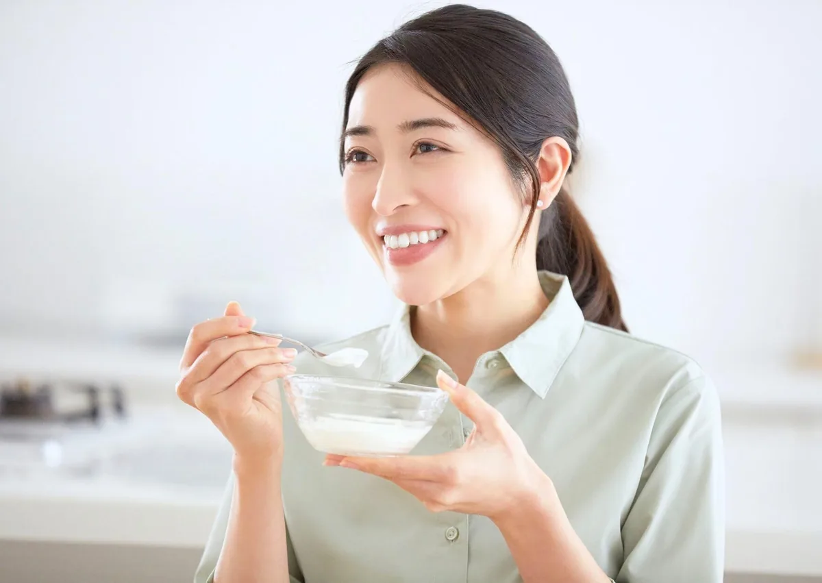 Woman eating yogurt as a soft food option after dental implant surgery.